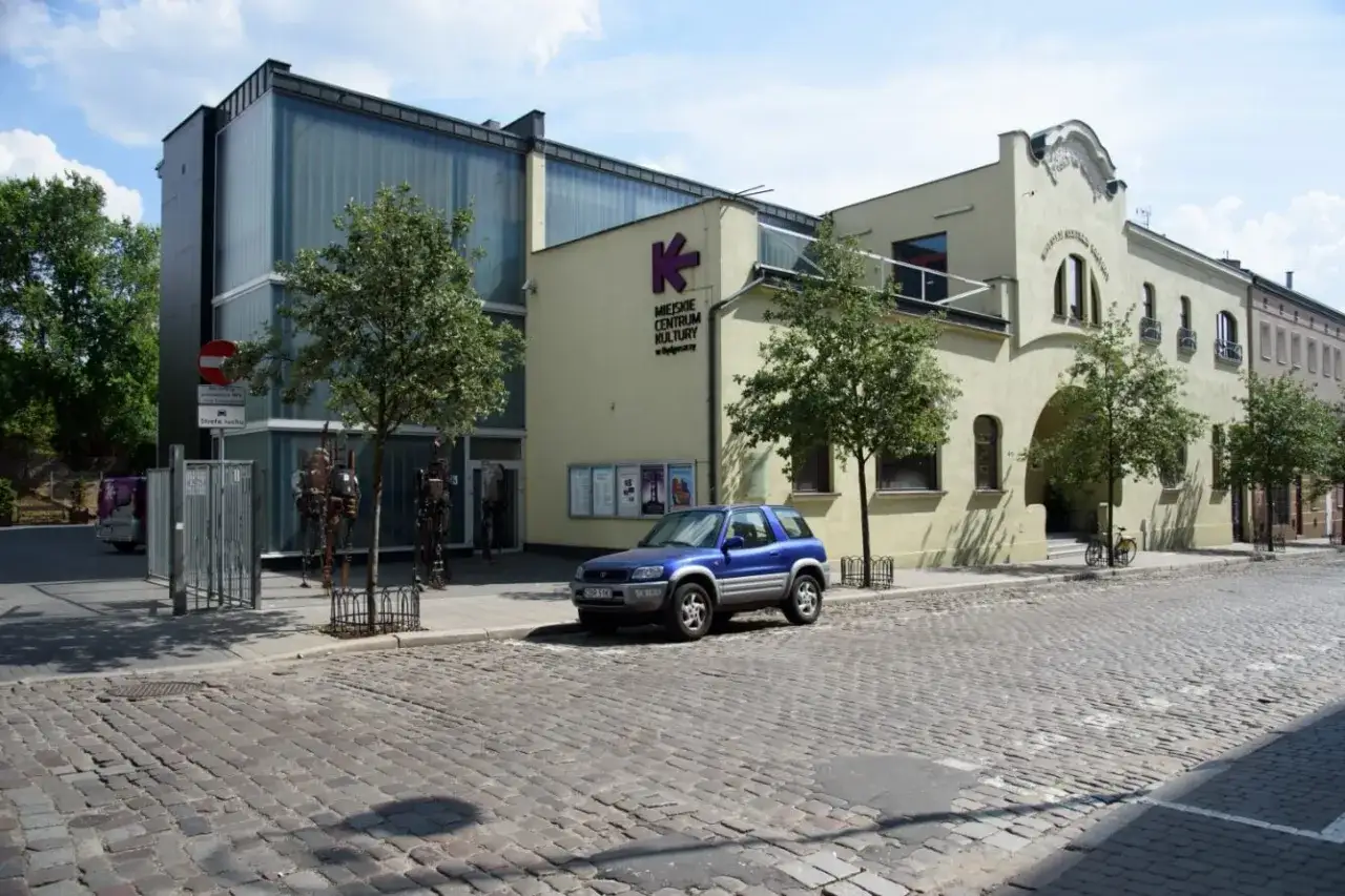 Miejskie Centrum Kultury w Bydgoszczy zaprasza na bydgoszcz wydarzenia kulturalne. Przed budynkiem stoi niebieski SUV.