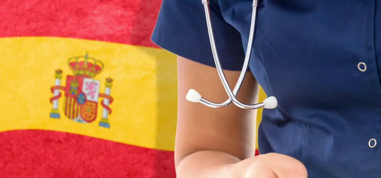 Un profesional de la salud con un estetoscopio frente a la bandera de Espa&ntilde;a. En Espa&ntilde;a, los d&iacute;as de reposo se pagan.