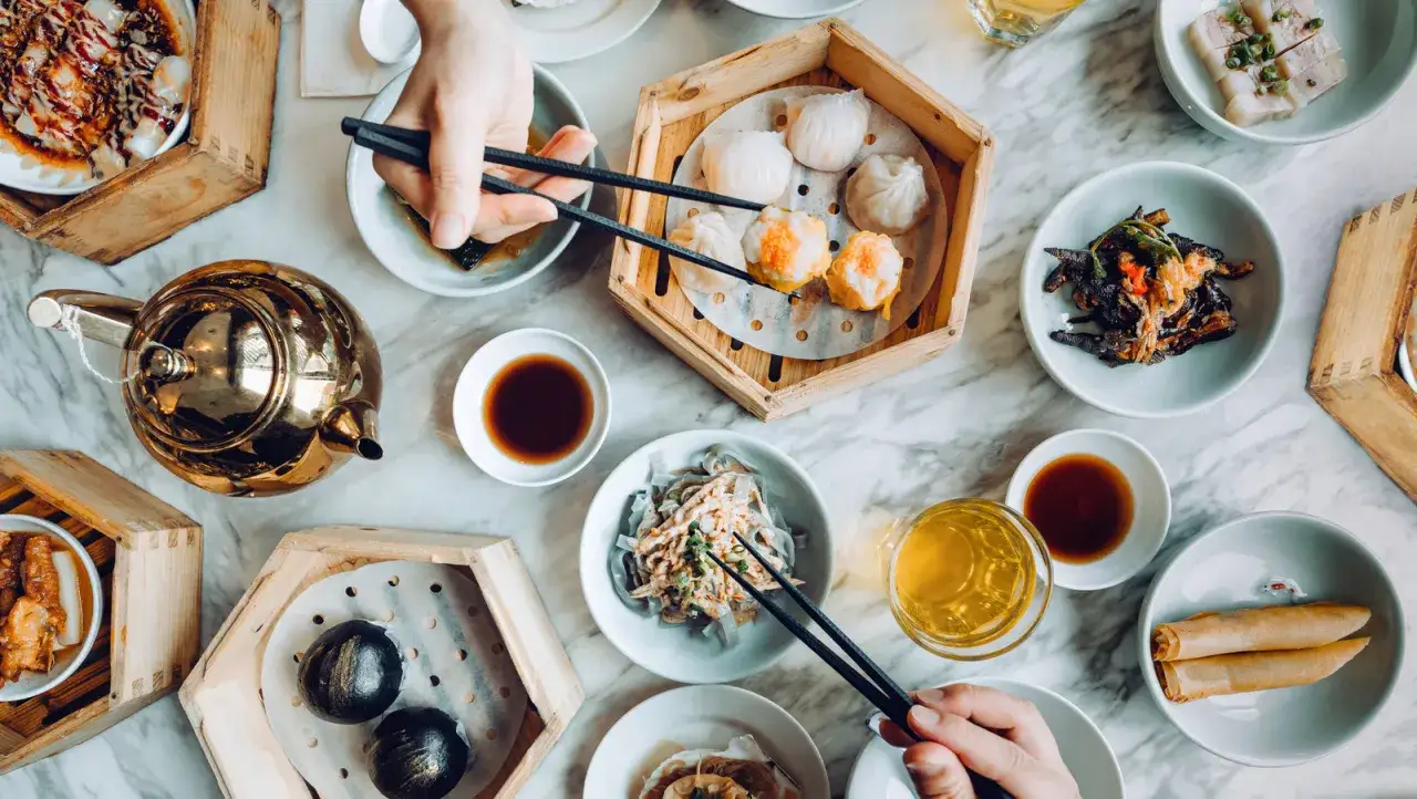 Stół pełen pysznego dim sum: pierożki, bułeczki, sajgonki i złoty czajniczek. Smacznego!