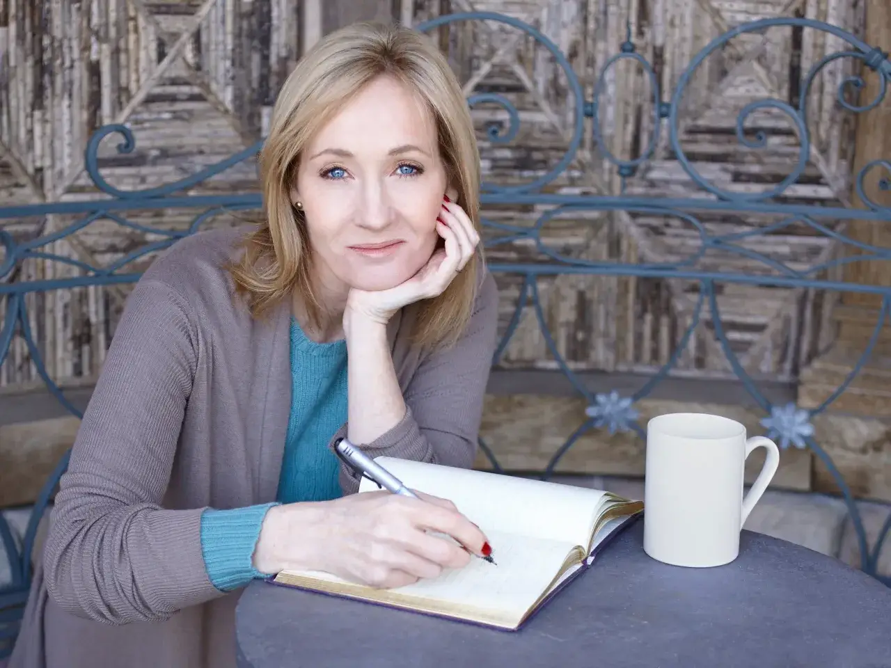 J.K. Rowling pisze w notatniku, być może tworząc nowe harry potter ciekawostki. Obok stoi biały kubek.