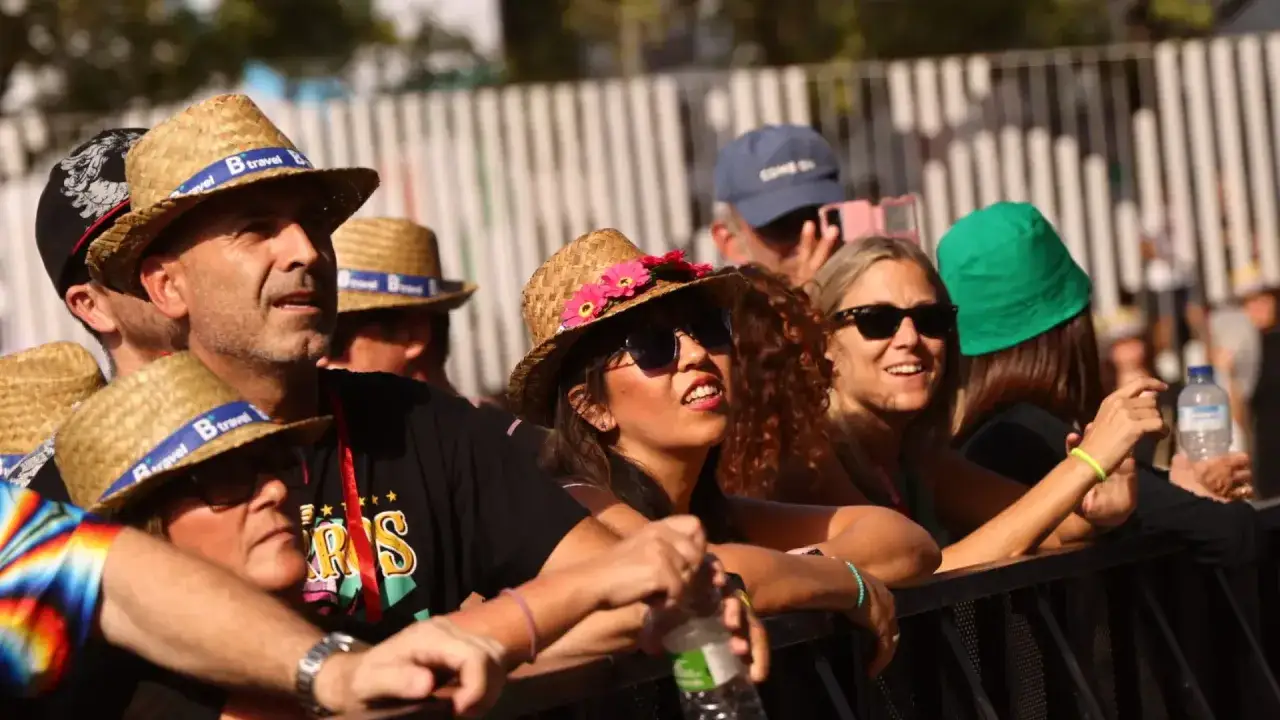 Gente disfrutando de un evento al aire libre, con sombreros de paja y gafas de sol. Se respira un ambiente festivo, como si fuera un vive latino zaragoza.