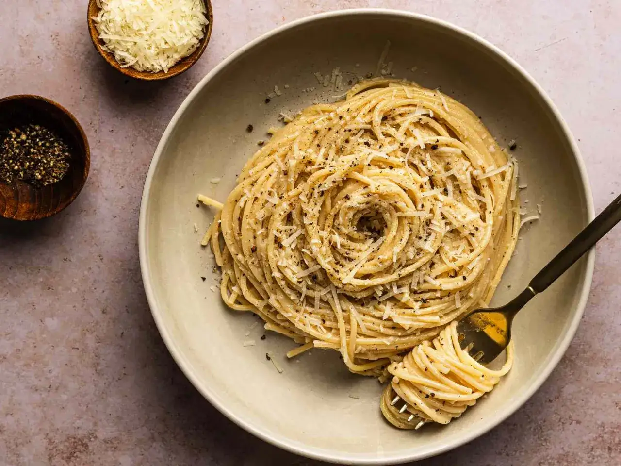Un piatto di pasta cacio e pepe, con spaghetti avvolti a spirale, guarniti con pecorino grattugiato e pepe nero macinato.