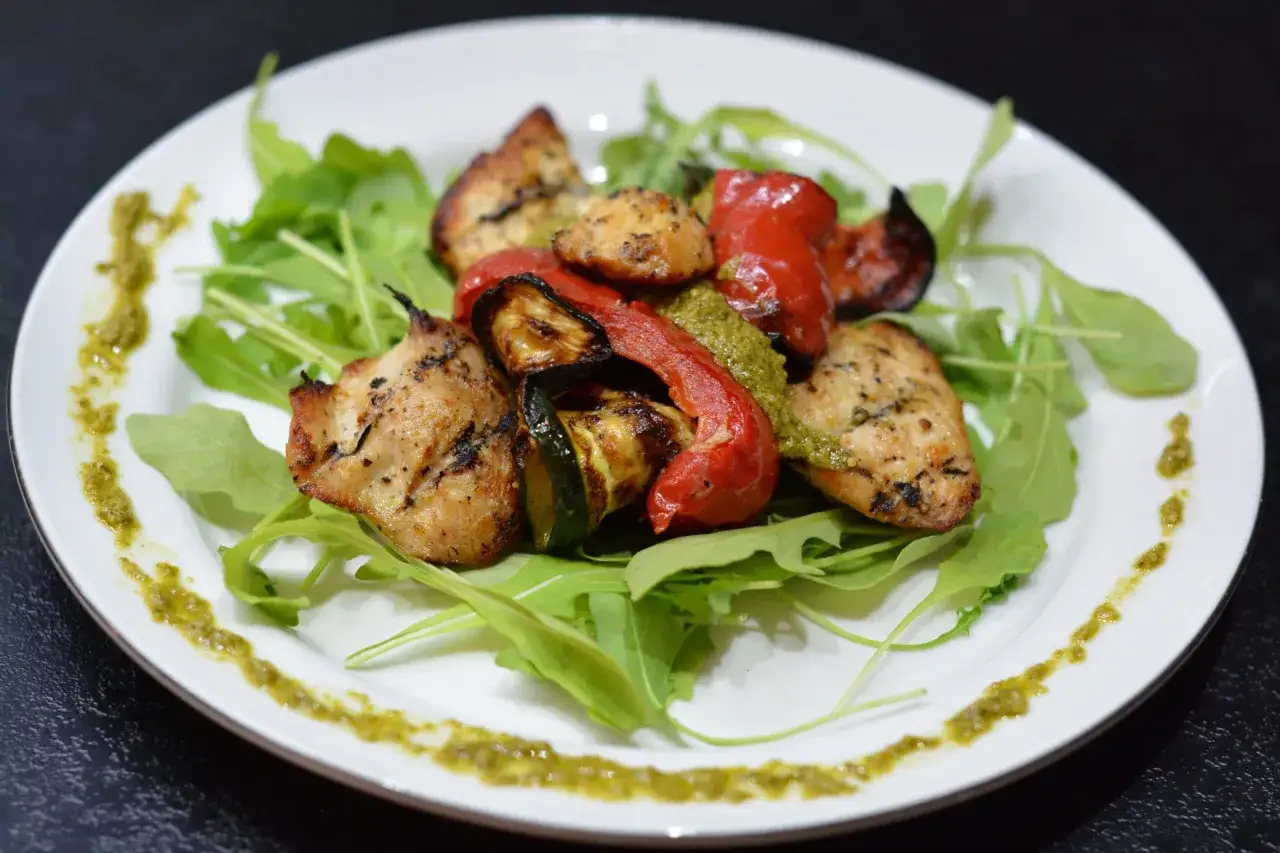 Prosta sałatka z piersią kurczaka, grillowanymi warzywami i rukolą, ozdobiona pesto.