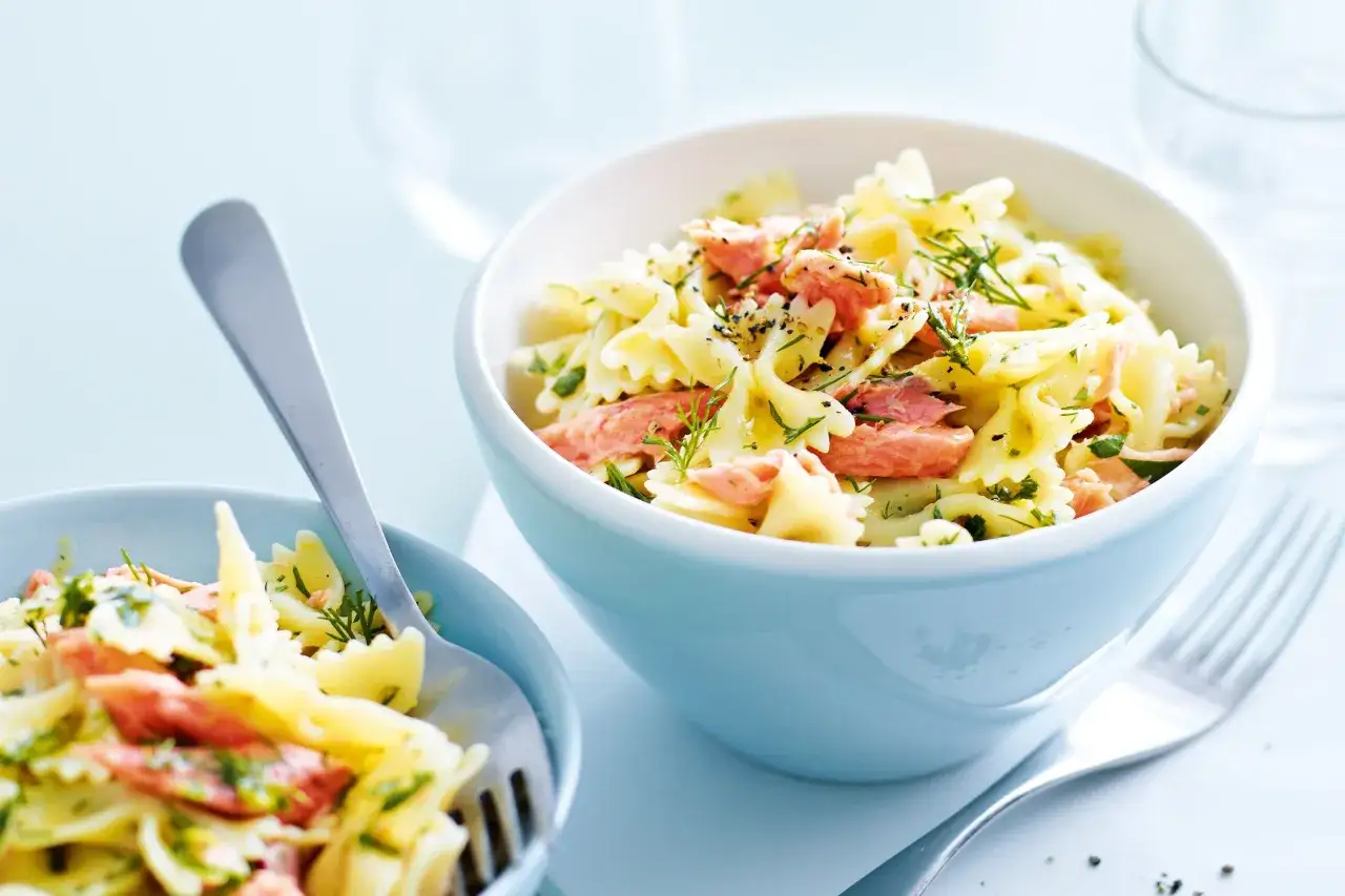 Två skålar med farfallepasta med laxsås, garnerad med dill och persilja. En gaffel ligger i den vänstra skålen.