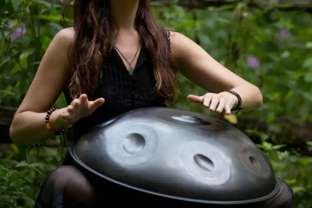 Kobieta gra na handpanie, jednym z mało znanych instrumentów muzycznych, w otoczeniu zieleni.