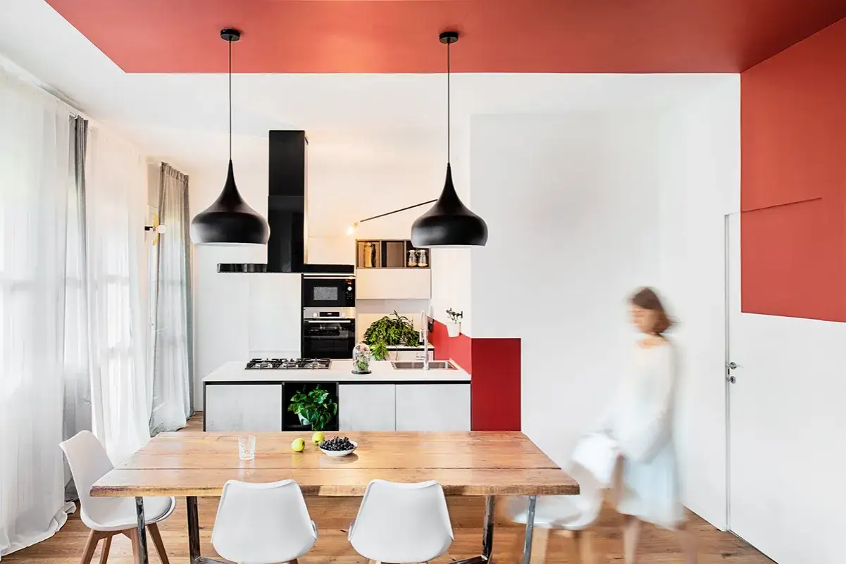 Soffitto rosso crea un bordo tra soffitto e parete, definendo lo spazio moderno con tavolo in legno e sedie bianche.