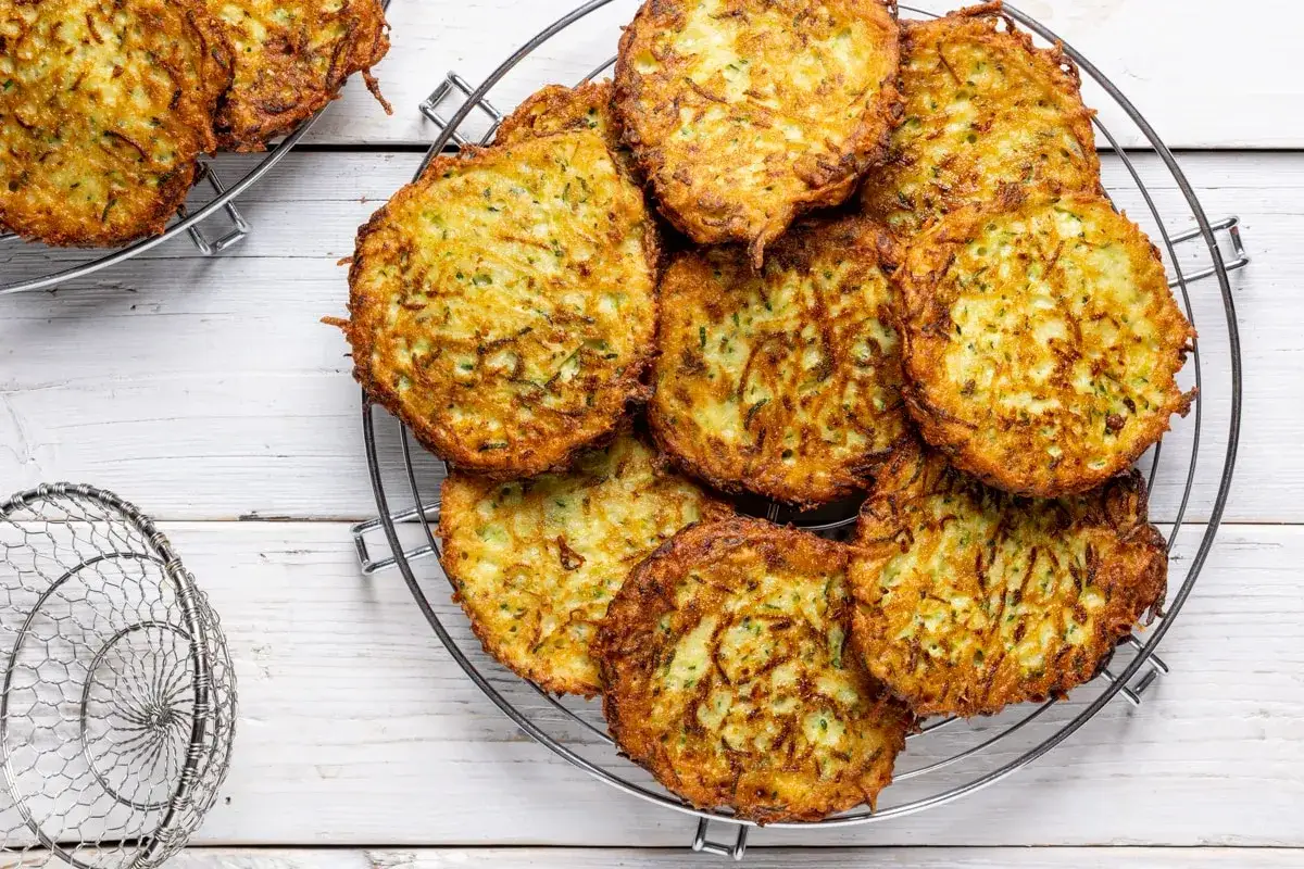 Un mucchio di rosti di zucchine dorati e croccanti su una griglia, pronti per essere gustati.