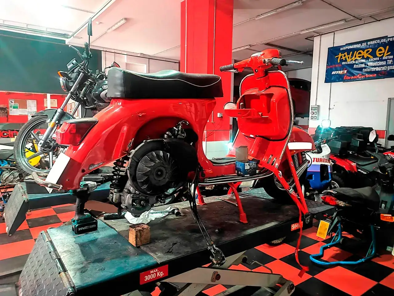 Taller mec&aacute;nico con Vespa roja y moto negra. Se discute el precio de reprogramar centralita moto.