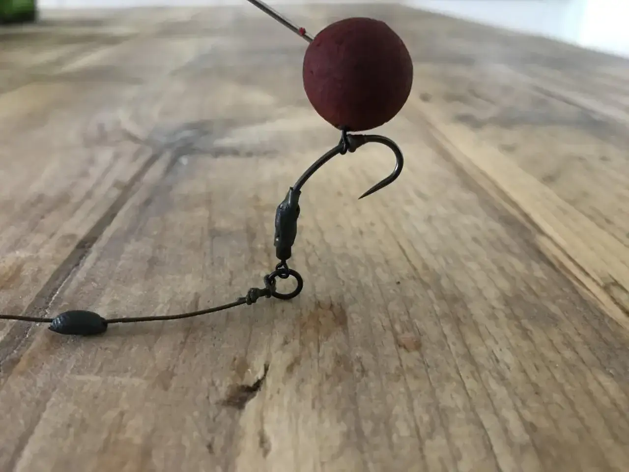 Ein Pop-up-Montage-Detail: Roter Köderball auf einem Haken, bereit für den Fang.