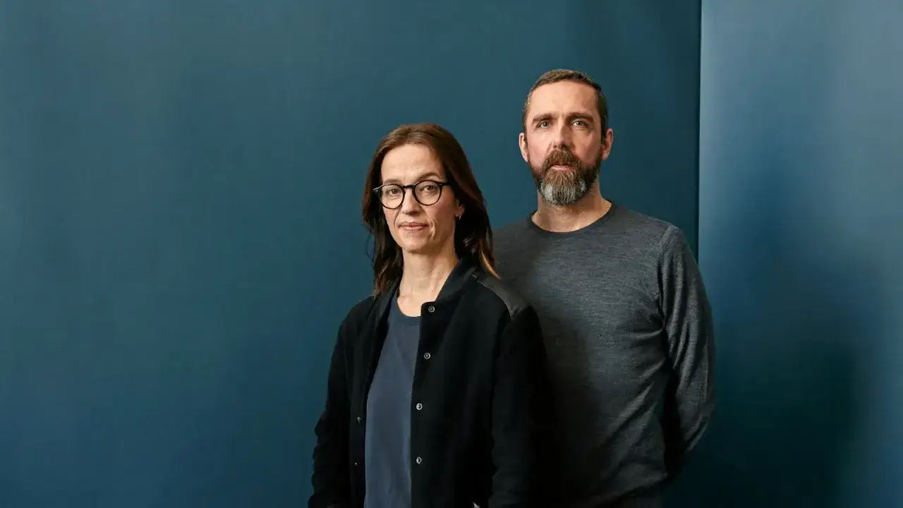 Ein Mann mit Bart und eine Frau mit Brille stehen vor einem blauen Hintergrund. Sie k&ouml;nnten die Hauptdarsteller der neuen **exit serie** sein.