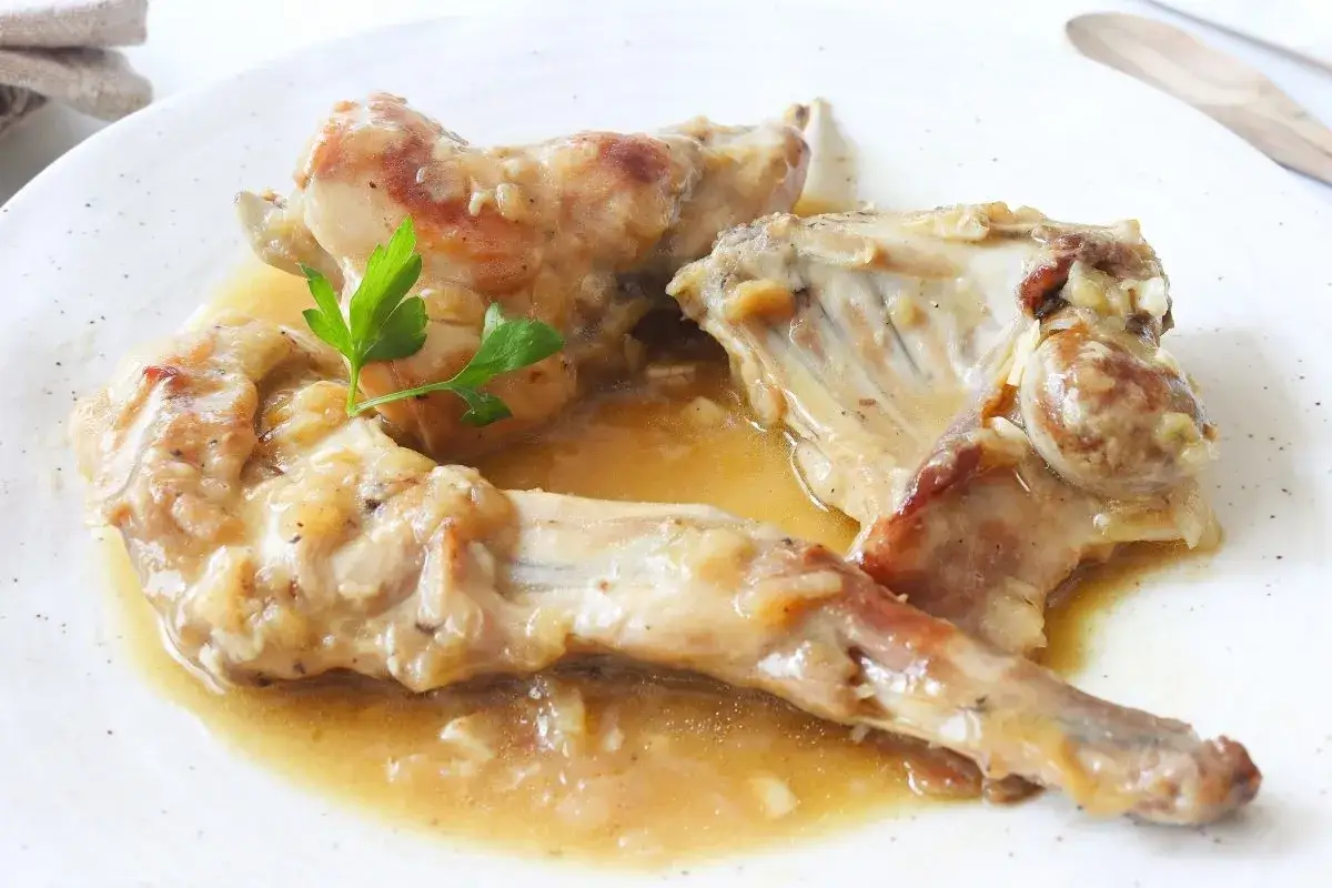 Delicioso conejo en salsa, servido en un plato blanco con perejil fresco.