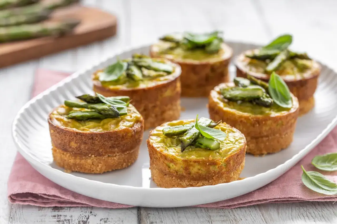Sei flan di verdure, con asparagi e basilico fresco, serviti su un piatto bianco.