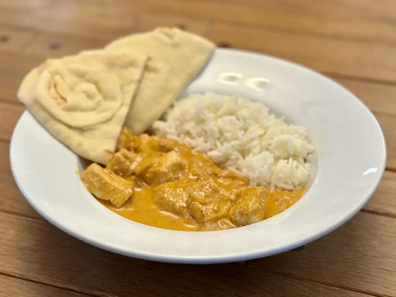 Pyszne chicken tikka masala z ryżem i chlebkiem naan na białym talerzu.
