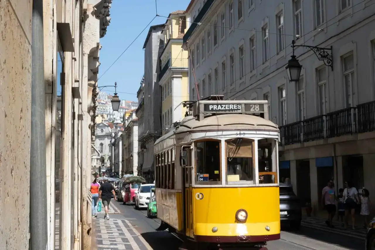 Żółty tramwaj w Lizbonie, uliczka z budynkami i ludźmi. Pamiętaj, czego nie robić w Portugalii, by cieszyć się podróżą.