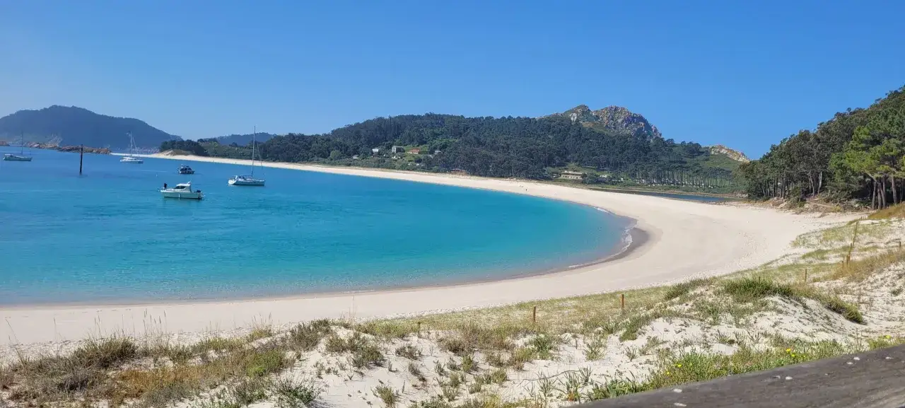 Aguas turquesas y arena blanca en la playa de las barcas, con veleros y barcos de recreo navegando plácidamente.