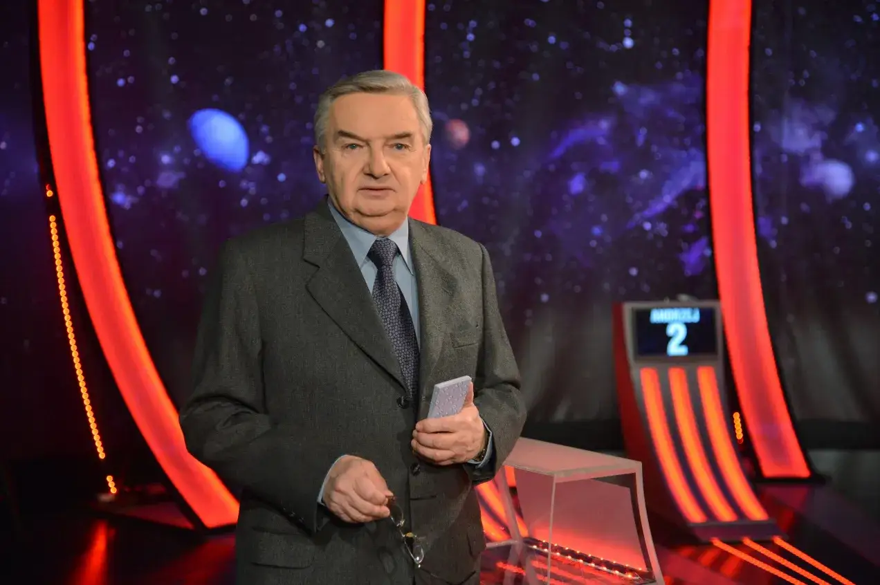 Starszy pan w garniturze trzyma karty, gotowy do gry w