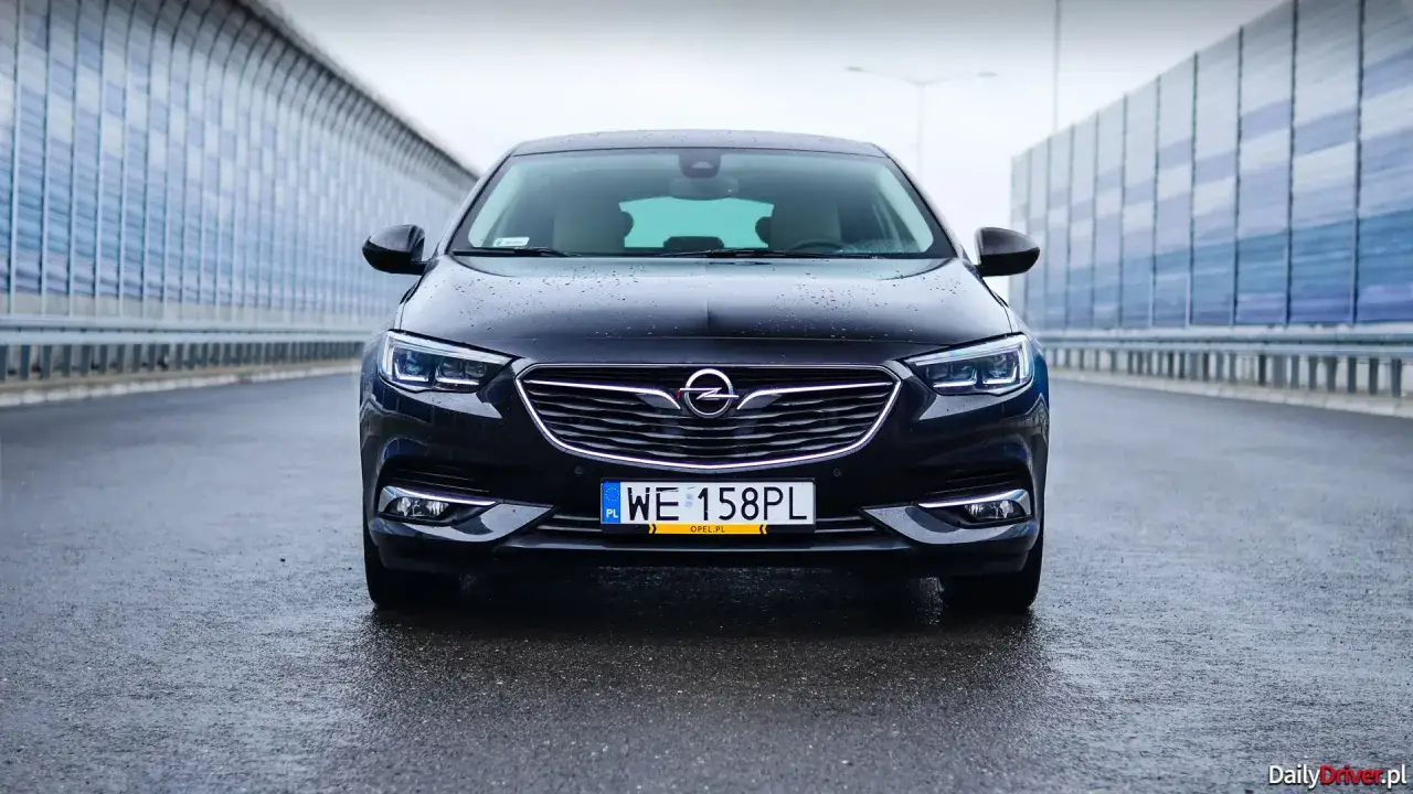 Czarny Opel Insignia 2.0 CDTI na mokrej drodze. Wiele osób szuka opinii o tym modelu przed zakupem.