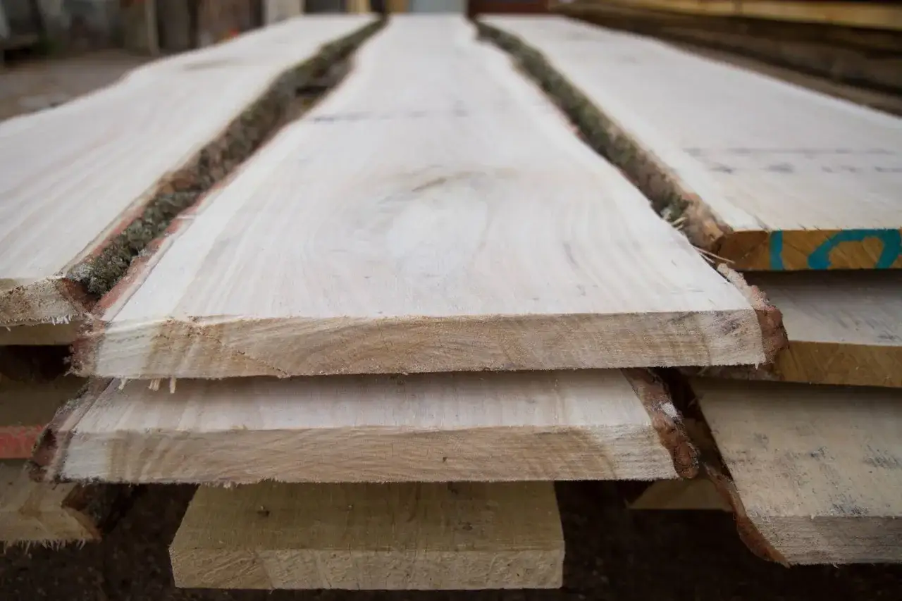 Tavole di legno grezzo impilate, con la corteccia ancora presente, pronte per il processo di stagionatura che ne assicura la durabilità.