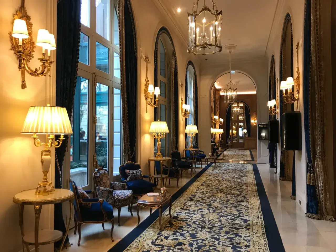 Elegancki korytarz hotelu Ritz w Paryżu, z luksusowym dywanem, złotymi lampami i zabytkowymi meblami.