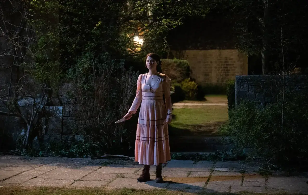 Eine Frau in einem rosafarbenen Kleid steht im Dunkeln mit einem Messer in der Hand. Ein bedrohlicher Moment in diesem men film.