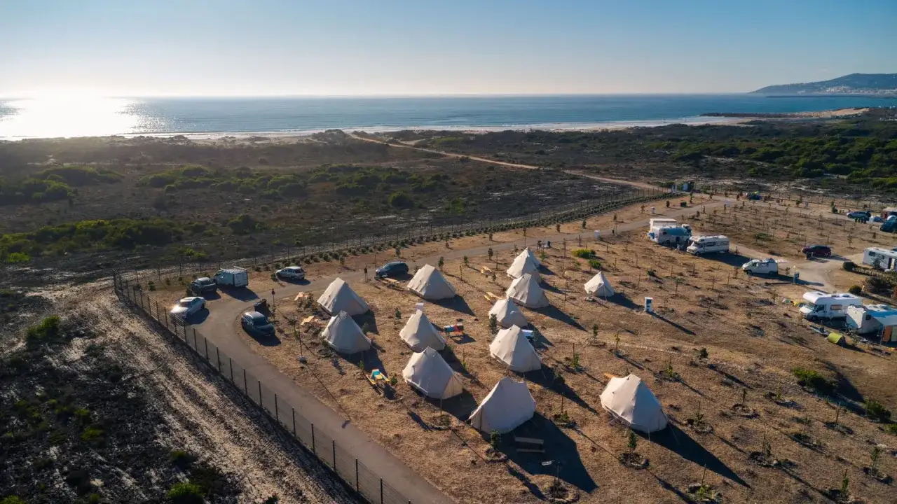 Glamping en el norte de Portugal, con tiendas tipo bell y autocaravanas junto a la playa bajo un cielo azul.
