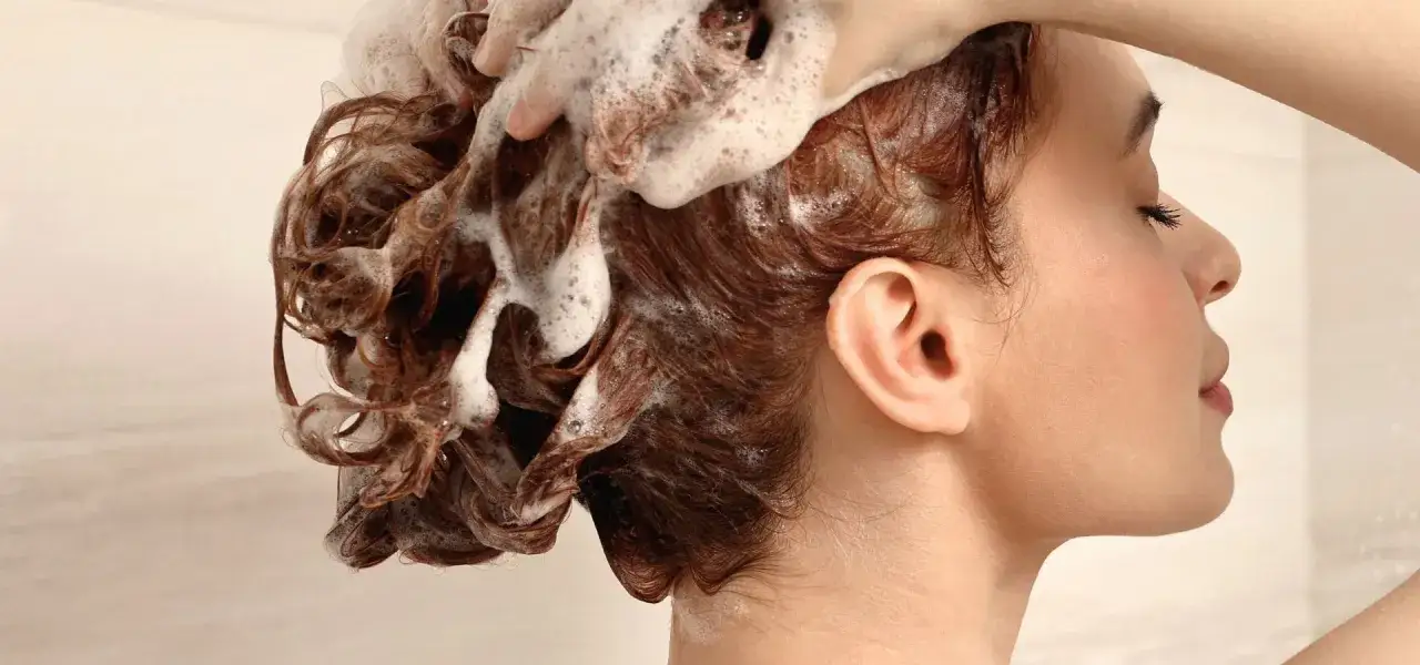 Una mano masajea espuma en el cabello rizado y castaño durante un lavado de cabeza.