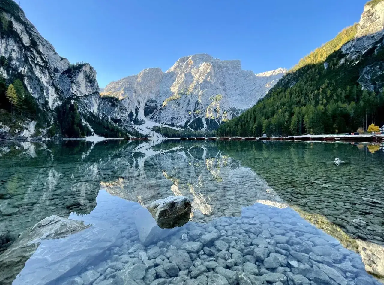 Der Pragser Wildsee spiegelt majest&auml;tische Berge und gr&uuml;ne W&auml;lder. Kleine Boote liegen am Ufer.