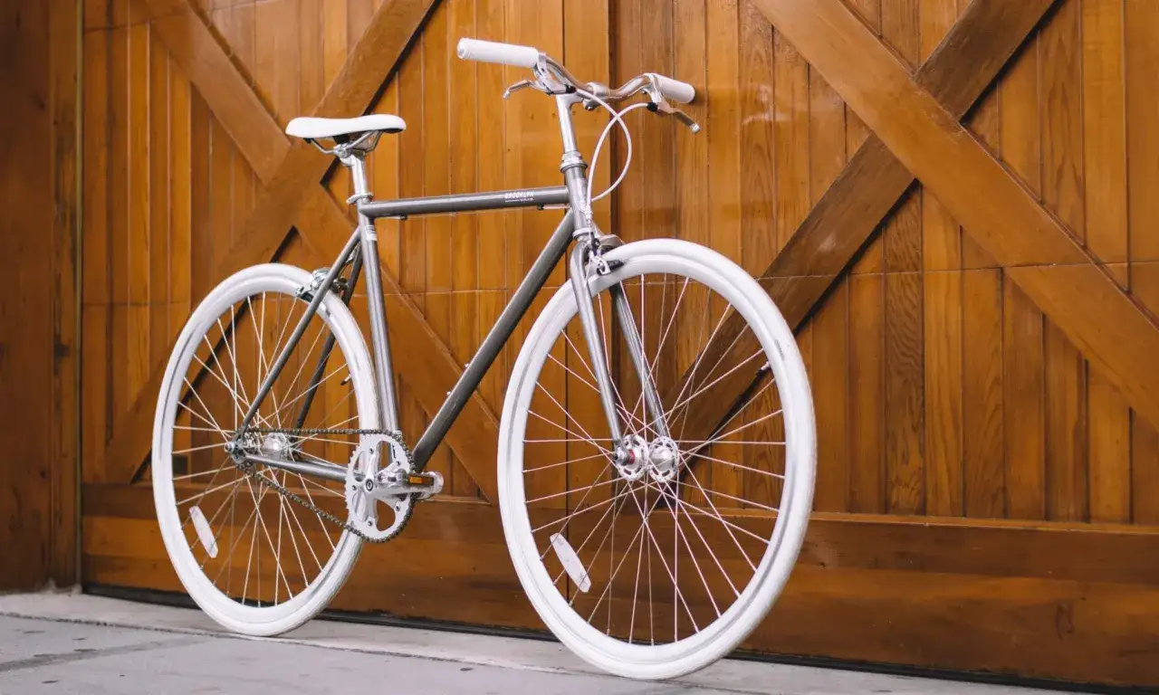 Ein schlichtes, graues Fahrrad mit wei&szlig;en Reifen und Sattel lehnt an einer Holzt&uuml;r. Das ist ein typisches Beispiel, was ist ein urban bike: praktisch und stilvoll f&uuml;r die Stadt.