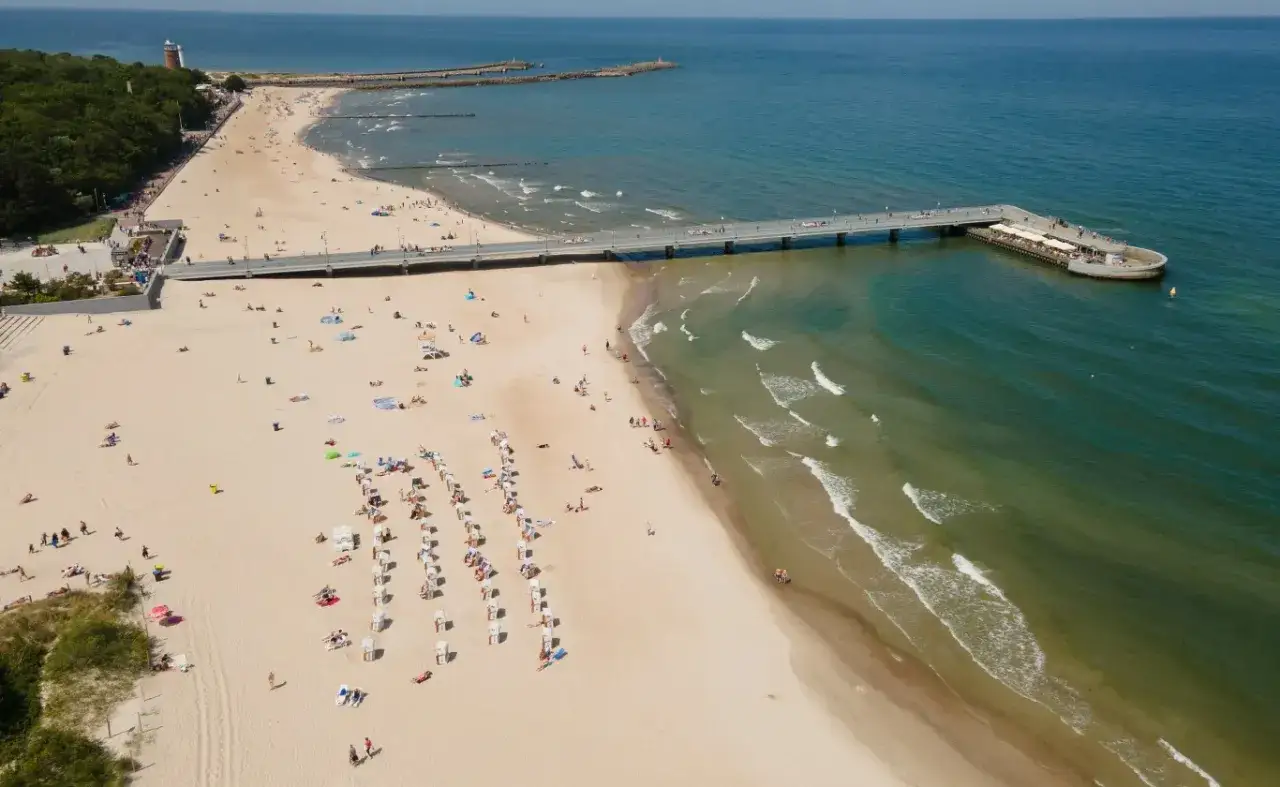 Słoneczny weekend majowy nad morzem. Ludzie odpoczywają na plaży, spacerują po molo i kąpią się w morzu.