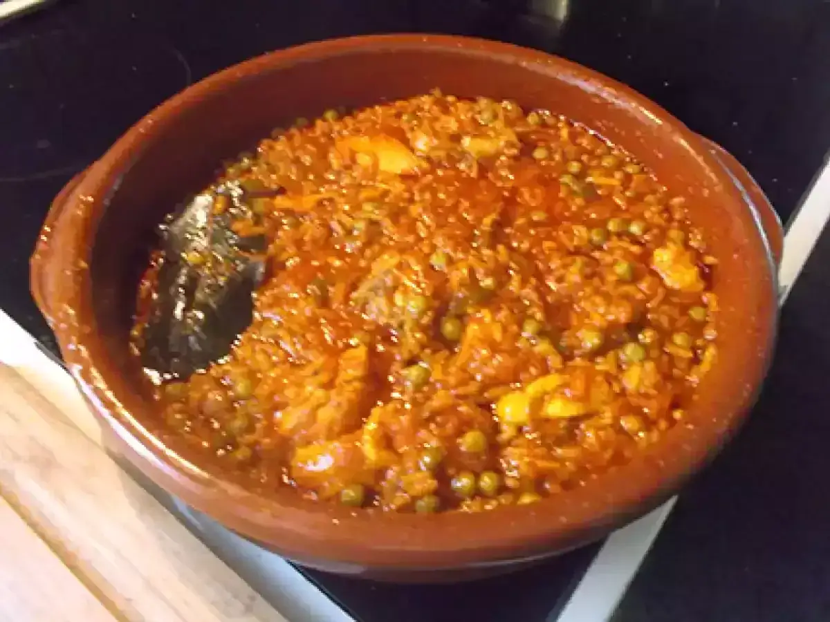 Un delicioso arroz con pollo en cazuela de barro, con guisantes y trozos de pollo jugoso.