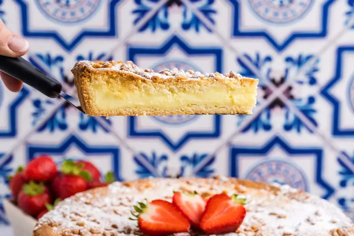 Ein Stück Torta della Nonna mit cremiger Füllung wird serviert. Frische Erdbeeren und Puderzucker zieren den Kuchen.