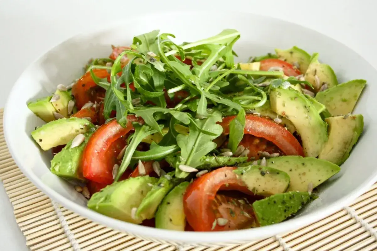 Ensalada fresca con rodajas de qué es el aguacate, tomates rojos, rúcula y semillas de girasol.