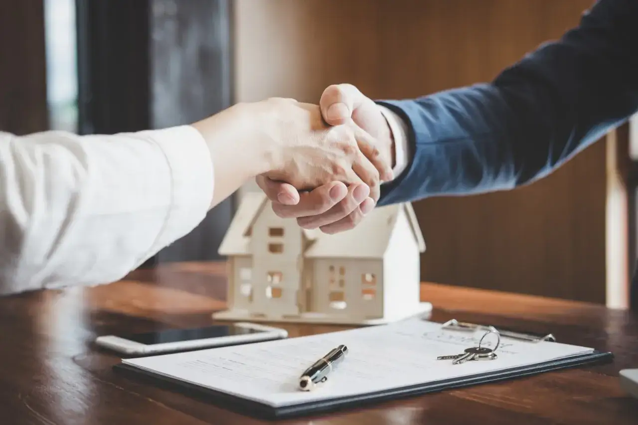 Accordo raggiunto per la surroga mutuo. Due mani si stringono su un tavolo con una casa in miniatura, chiavi e contratto.