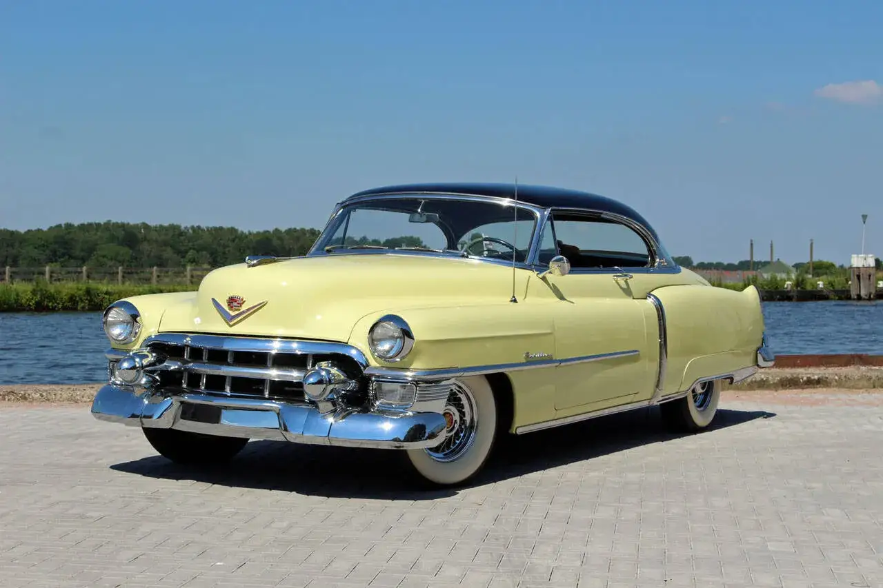 Ein gelber Cadillac Coupé mit schwarzem Dach steht am Wasser.