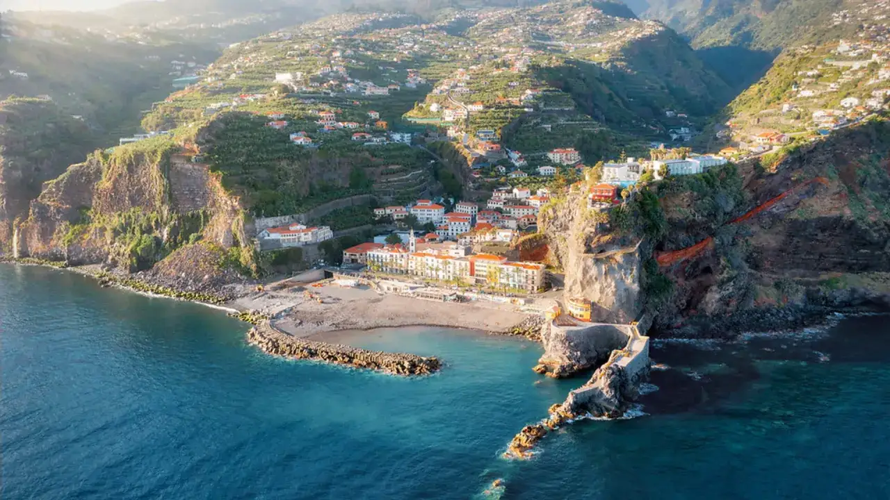 Blick auf eine Küstenstadt auf Madeira mit terrassierten Hängen. Perfekt für die Reisezeit, wenn die Madeira Klimatabelle mildes Wetter verspricht.