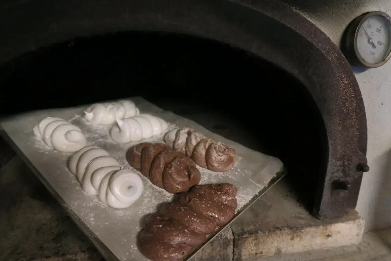 Des meringues blanches et chocolat&eacute;es sont en cours de cuisson dans un four rustique.