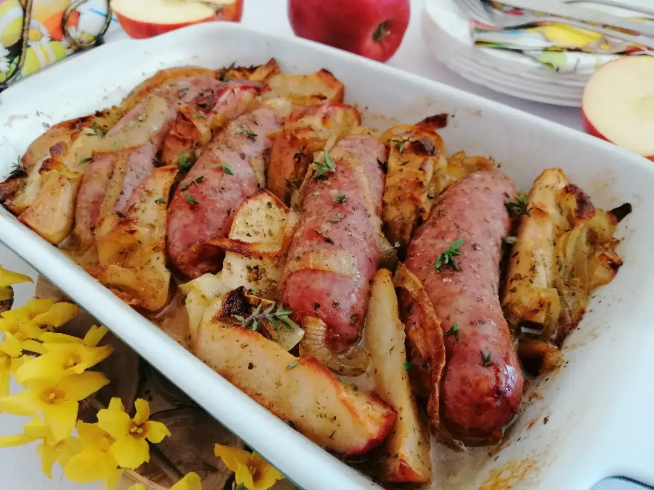 Pyszna biała kiełbasa pieczona z jabłkami i ziołami w naczyniu żaroodpornym.