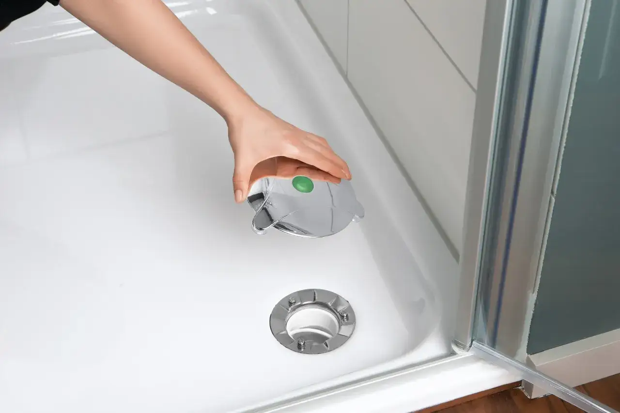Hand setzt den glänzenden Abflussdeckel auf die Duschwanne. Der Einbau der Duschwanne ist fast abgeschlossen.