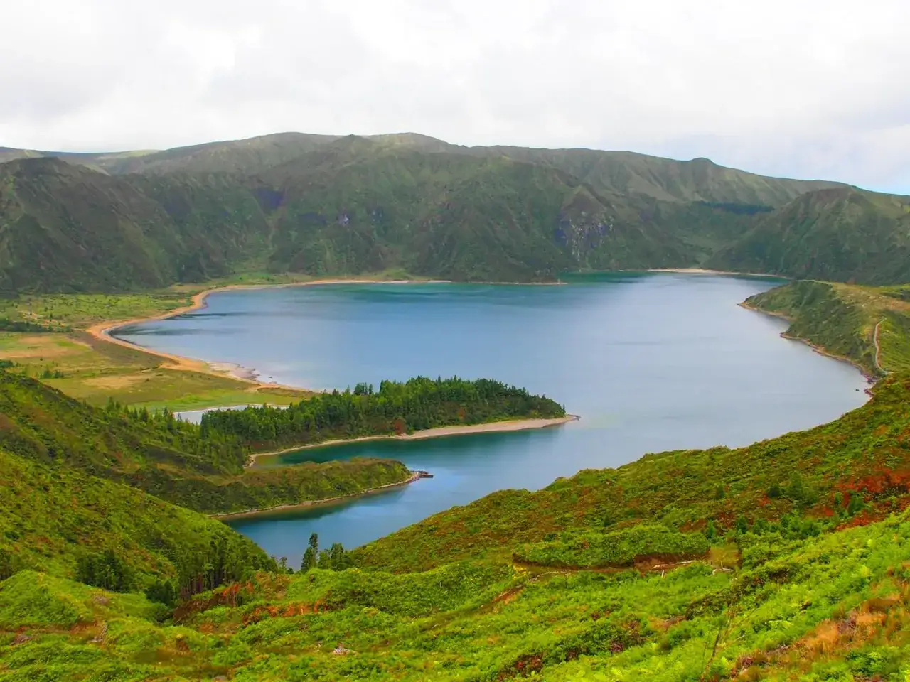 Vista panorámica de la Lagoa do Congro, un lago azul rodeado de colinas verdes exuberantes y vegetación densa.