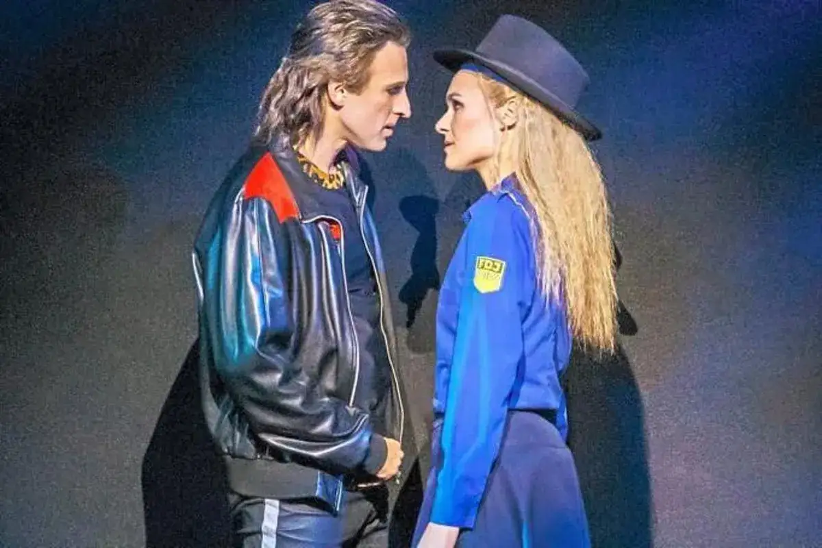 Udo Lindenberg Bilder: Ein Mann mit Lederjacke und eine Frau im blauen Outfit mit Hut blicken sich an.