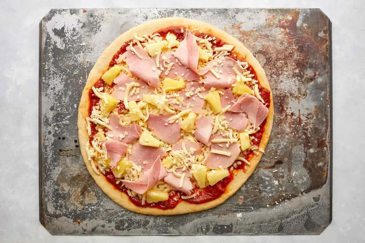 Pizza z ananasem i szynką, gotowa do pieczenia na starej blasze.