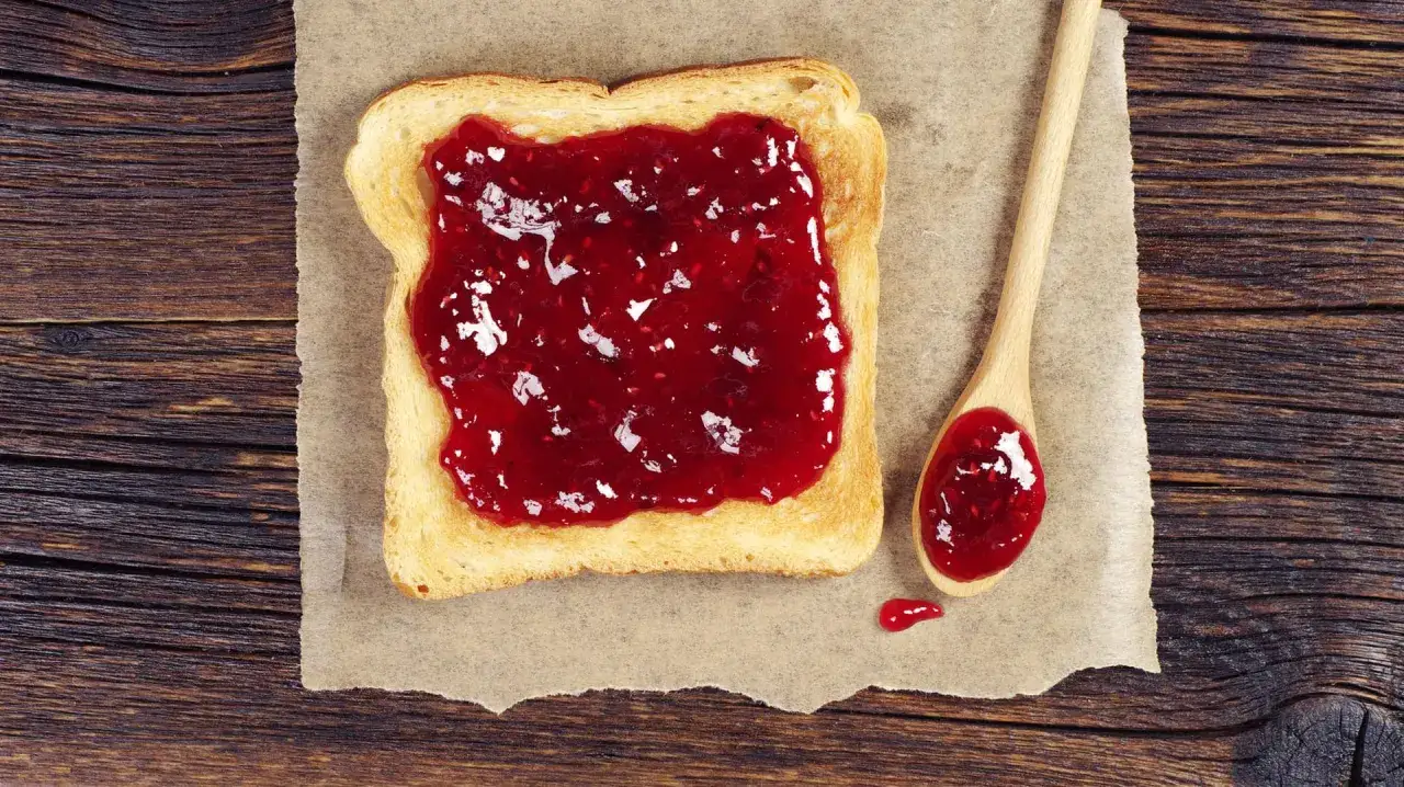Ger&ouml;stetes Brot mit leckerer Marmelade, die aussieht, als w&auml;re sie mit Gelierzucker selber gemacht. Eine Holzl&ouml;ffel liegt daneben.