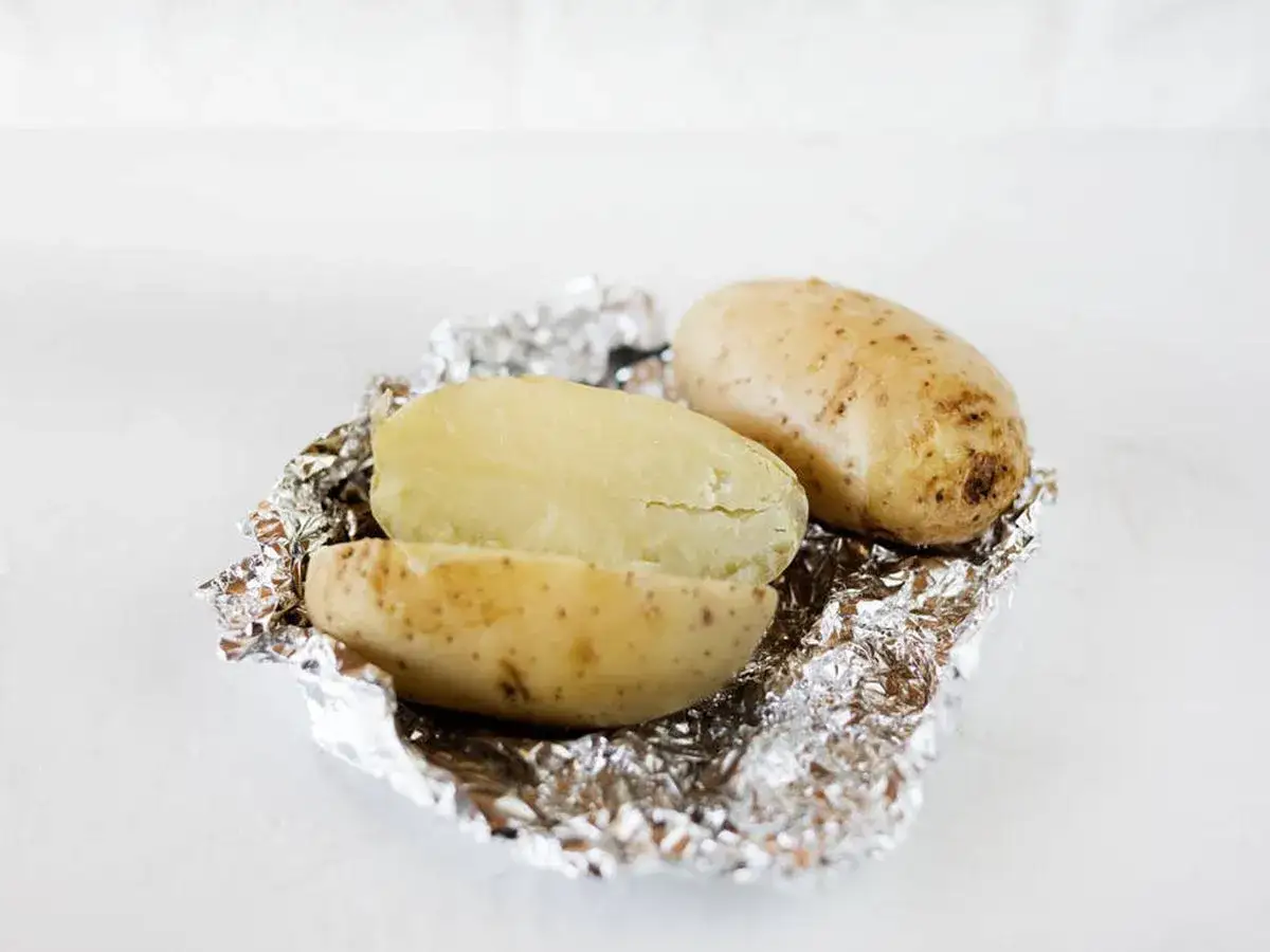 Dos patatas al microondas, una entera y otra partida por la mitad, sobre papel de aluminio.