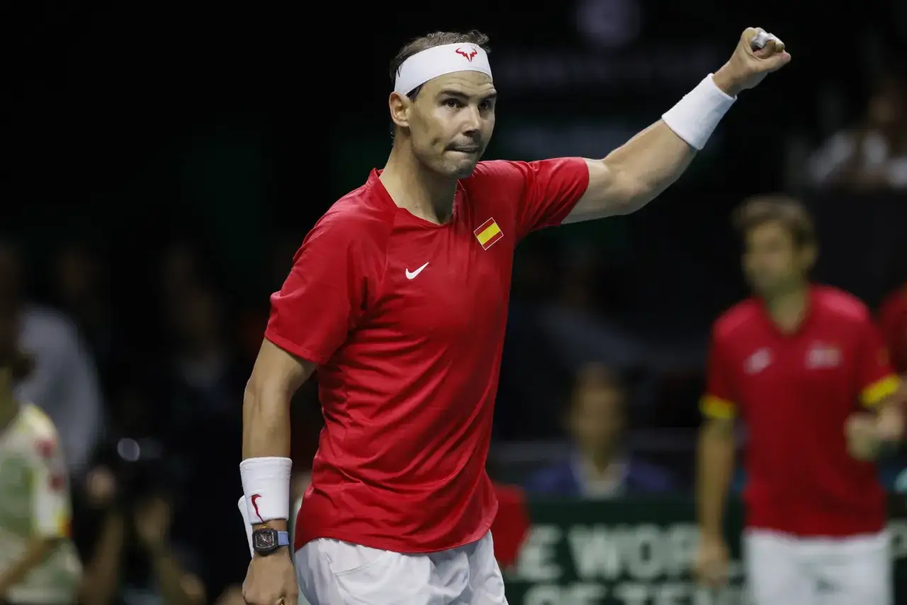 Rafael Nadal w czerwonej koszulce z flagą Hiszpanii, zaciśnięta pięść w geście triumfu. Jego majątek to wynik lat ciężkiej pracy.
