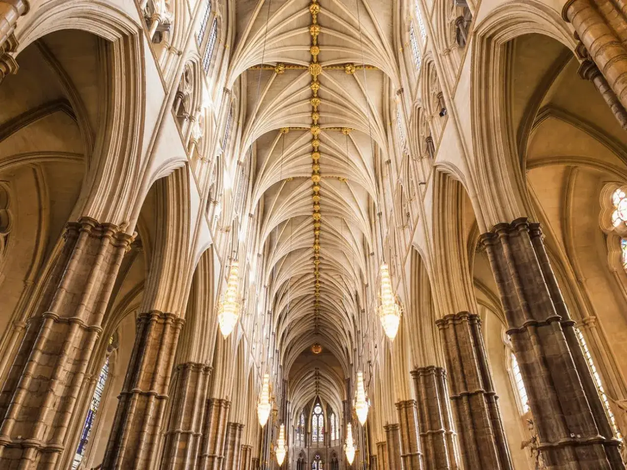 Vue plongeante sur les voûtes gothiques et les colonnes imposantes de l'abbaye de Westminster, illuminées par des lustres élégants.
