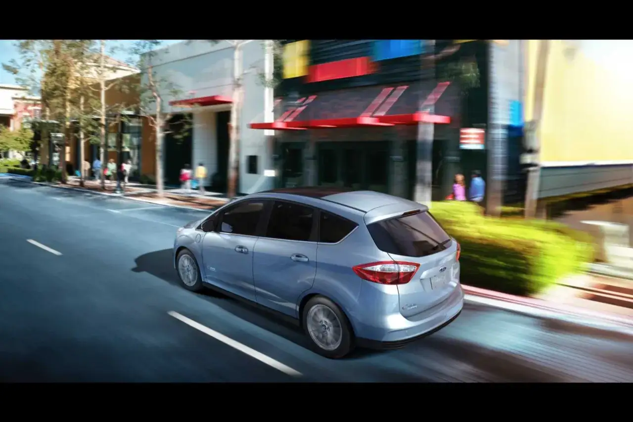 Ein hellblauer Ford C-Max Energi Plug-in Hybrid fährt durch eine belebte Stadtstraße.