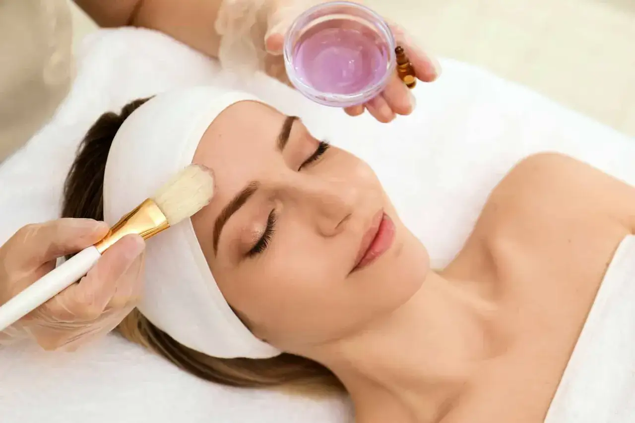 Application d'un soin pro power peel sur le visage d'une femme d&eacute;tendue, avec une brosse douce et un liquide violet.