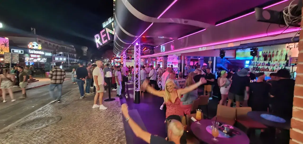 Nachtleben in Albufeira: Menschen tanzen und feiern auf der Partymeile unter bunten Lichtern.