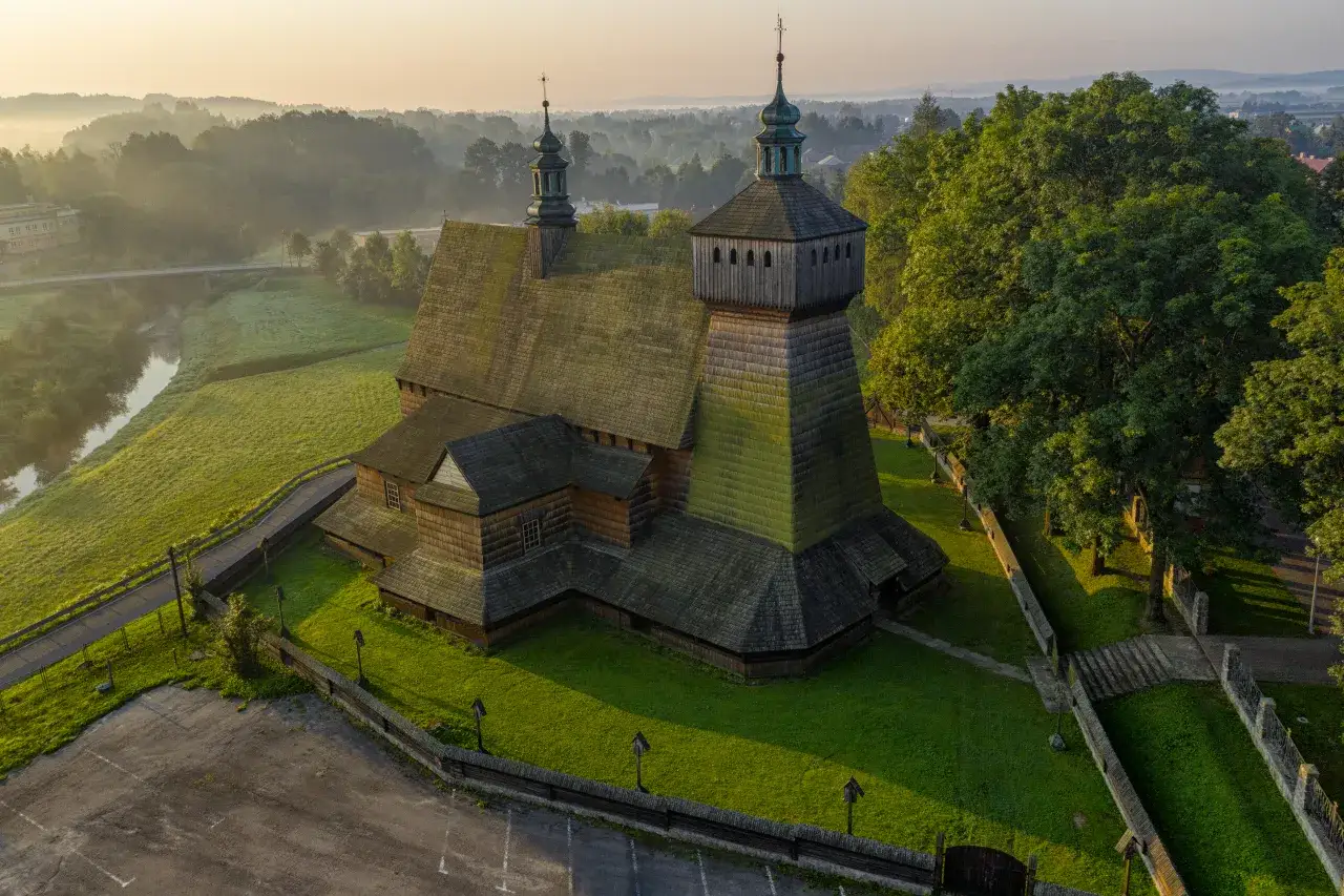 Drewniana cerkiew z zielonymi kopułami, otoczona zielenią i mgłą. Idealne miejsce, by zobaczyć, co zwiedzić na Podkarpaciu.