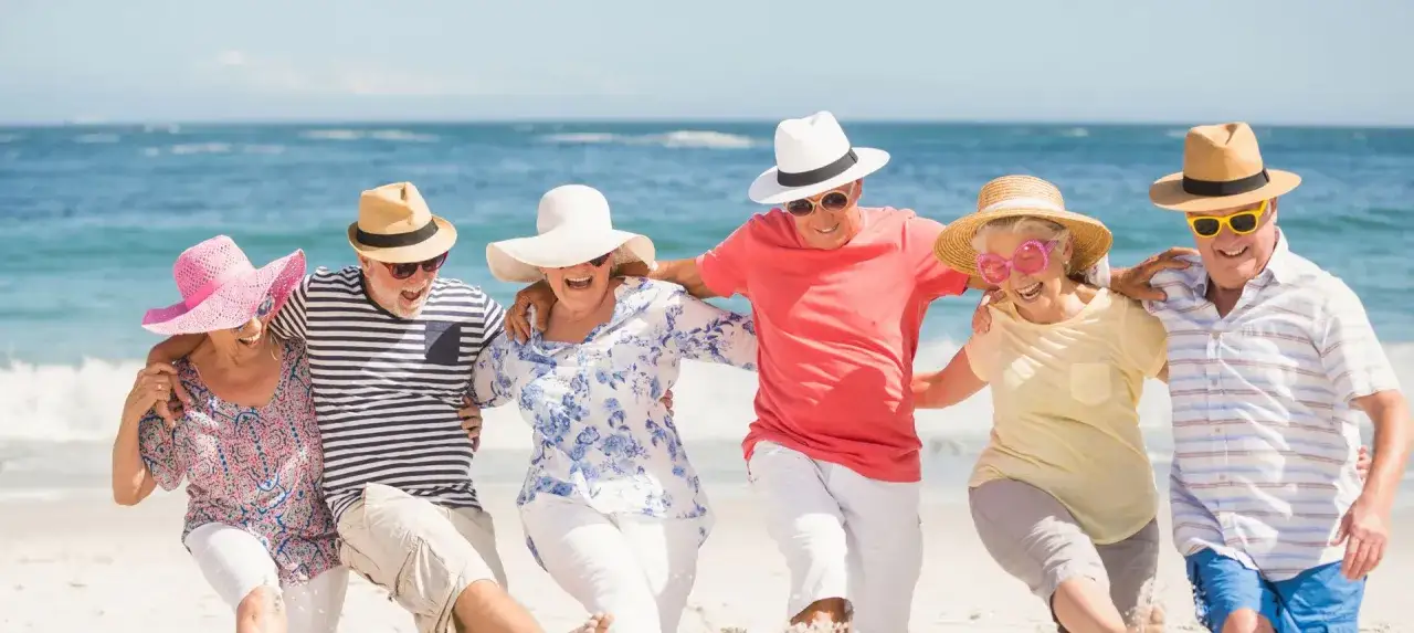 Szczęśliwi seniorzy na plaży, cieszący się słońcem i morzem. Idealne tanie wczasy dla seniora za granicą, pełne radości i beztroski.